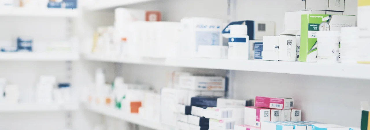 Shelves lined with various boxes and packages of medication in a pharmacy or medical supply room, organized but not labeled in detail.