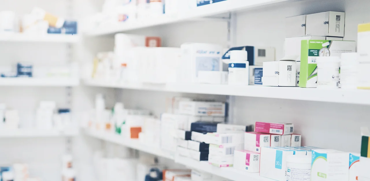 Shelves lined with various boxes and packages of medication in a pharmacy or medical supply room, organized but not labeled in detail.