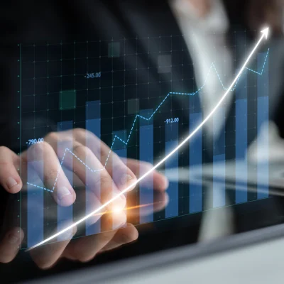 Person uses a tablet with a digital graph overlay showing upward-trending data, indicating financial or business growth.